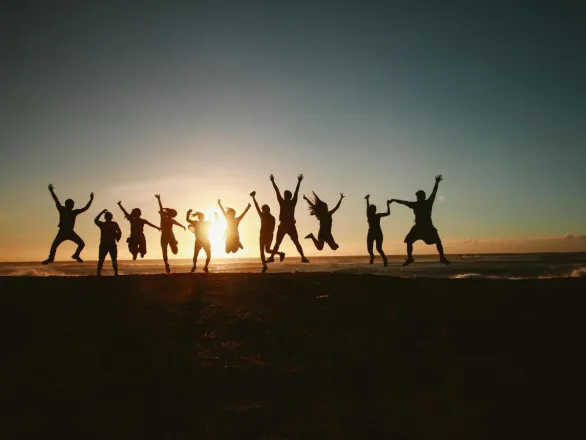 Silhouette of a group of friends jumping on a beach at sunset, expressing joy and freedom.